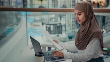 Tesettürlü Müslüman bir kız serbest çalışan iş kadını. İş yerindeki bilgisayarın kontrol belgelerinde çalışıyor. Bilgisayardaki verileri girin.