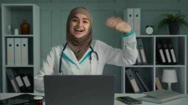 Webcam görüntüsü mutlu genç doktor kadın pediyatrist psikoterapist hastayı online psikoloji seansında selamlıyor kameraya bakıp el sallıyor görüntülü sohbet ve uzaktan sağlık danışmanlığı ile konuşuyor.