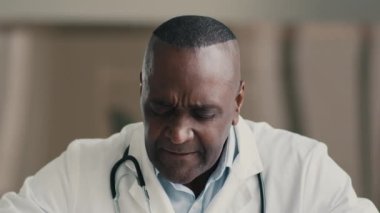 Aşırı yüklenmiş yorgun hasta adam, Afrikalı Amerikalı doktor, hastanede çalışıyor, dokunmatik şakaklarda, yorgunluk, migren, baş ağrısı, aşırı çalışma, koronavirüs salgını.