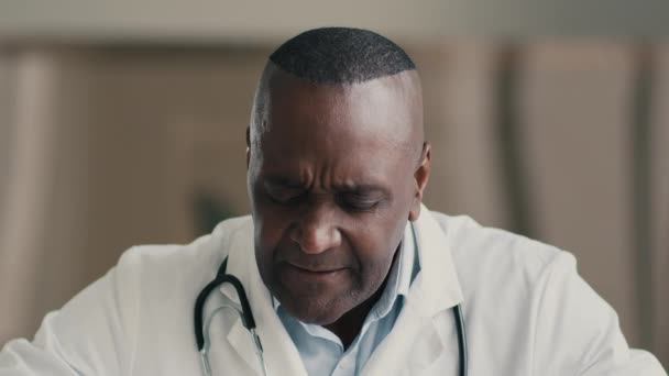過重疲労した病気の男性アフリカ系アメリカ人医師が病院のタッチ寺院で働いている疲労片頭痛の病気が頭痛の健康上の問題を強打するのを感じる原因コロナウイルスのパンデミック — ストック動画