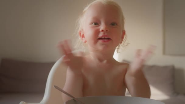 귀엽고 귀여운 아기가 식탁에 앉아서 갓난아기 딸이나 아들에게 박수를 보내고 — 비디오