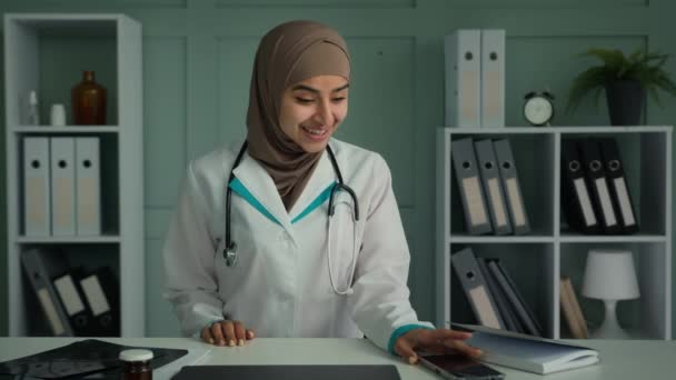 ポートレート幸せな医師イスラム教徒の女性でヒジャーブ女性医師婦人科若い世代のアラビア民族学生は 医療インターンシップの終わりを祝う携帯電話のダンスのお祝いに良い通知を読みます — ストック動画
