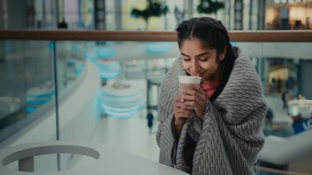快乐宁静的阿拉伯裔惊慌失措的年轻女学生坐在咖啡馆餐厅里喝着热咖啡因饮料穿着保暖毛毯喝着香气咖啡香草茶放松茶点的概念 — 图库视频影像