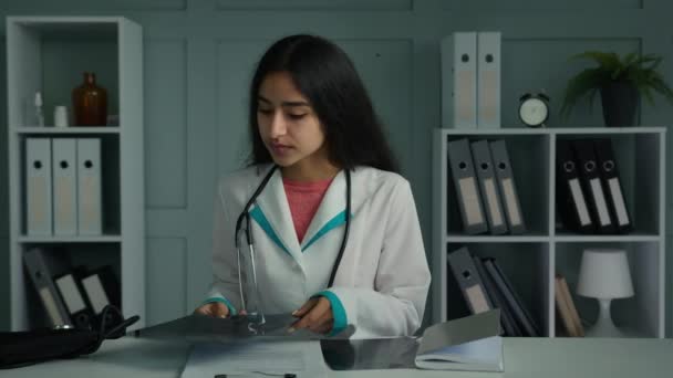 医生护士年轻女性医生医护人员坐在诊所柜台前开始工作日整理纸质文件 填写医疗清单 并在注册日志上填写X光结果 — 图库视频影像