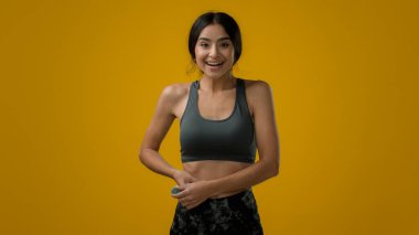 Stüdyo sarı arka planda Etnik kadın Hintli sporcu bayan atlet kadın bel ölçüsünde vücut şekli bant kontrolü diyet sporu diyeti sonucu zayıflama gülümsemesi