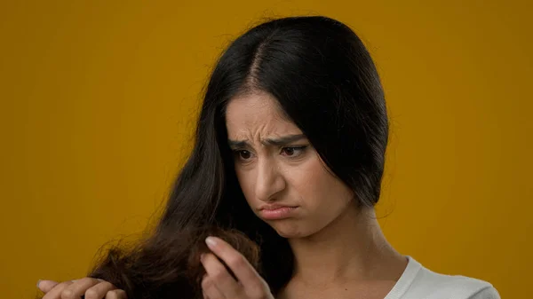 Depressed Indian ethnic woman girl female lady brunette looking at split ends of hairstyle worried feels upset about brittle damaged dry hair loss alopecia hormone problems or vitamins deficiency