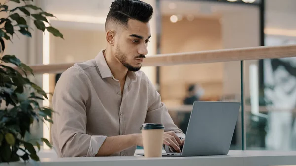 Indian Hispanic ethnic worker manager student businessman freelancer entrepreneur man guy typing business email sit at cafe table with laptop work drinking coffee distant working with computer online