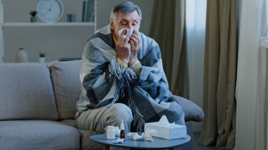 Sıcak battaniyeye sarılı hasta yaşlı adam peçeteyle hapşırmaktan acı çekiyor. Yaşlı hasta büyükbaba kötü ateş hastalığı belirtileri gösteriyor. Son sınıf erkeklerinin sağlık sorunları var.