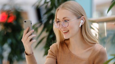 Yakın plan beyaz kadın blogger kablosuz kulaklık takıyor çevrimiçi kanal görüntüsü konferans konferansı sohbeti arkadaşlarıyla telefon kamerasına konuşan akıllı telefon uygulaması kullanarak