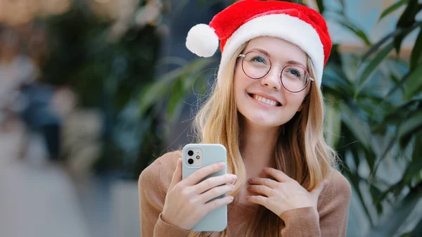 幸せな驚きの成功白人女性女の子女性で赤サンタクロースクリスマスの帽子と眼鏡を獲得で携帯電話の勝利を提供達成新年のお祝いの勝利割引オファーの勝利賞 — ストック写真