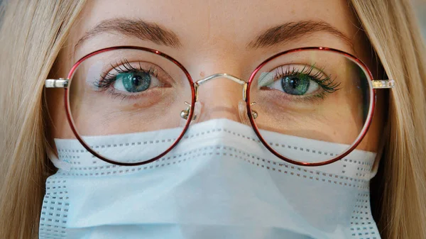 Extreme close up female face Caucasian girl woman with blue eyes wear glasses and medical mask female doctor nurse lab worker in respirator and eyewear looking at camera protection from covid pandemic