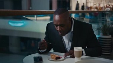 Etnik orta yaşlı iş adamı kafeterya ziyaretçisi turta yerken zevkini çıkarın. Başparmağınızı göstererek afro-yetişkin bir adamın kafeterya restoranında yediği pastayı afiyetle yiyin ve güzel bir tatlı yiyin.