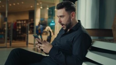 Kazanan İspanyol işadamı alışveriş merkezinde oturuyor akıllı telefon aygıtı kullanıyor sosyal ağlarda iyi haberler okuyor cep telefonunda internet satışları kazanıyor mutlu erkek çalışana iş teklifi geliyor.