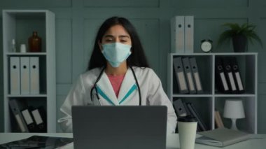 Maske takan genç bir tıp çalışanı web kamerası konferansında düşük sesli, güvenilmez internet bağlantısı sorunu yüzünden rahatsız olan dijital uygulama kullanıyor.