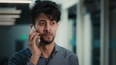 Hindistanlı genç 30 'lu yaşlardaki işadamı müşterisiyle cep telefonu görüşmesi yapıyor. Ofiste modern telefon teknolojisi kullanıyor. Uzaktan iletişim kuruyor.