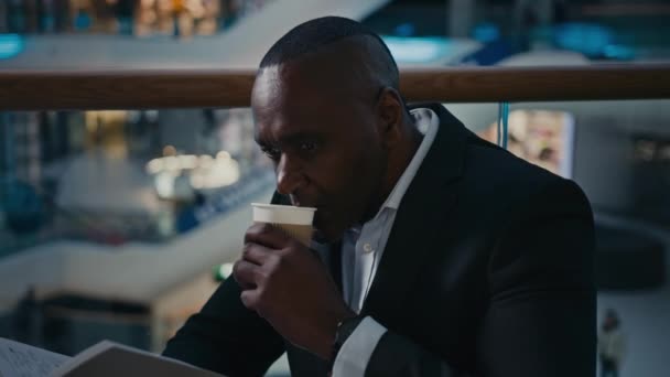 非洲裔男性商人雇主企业家在咖啡馆餐厅的桌子边喝茶 喝香浓的热咖啡 喝拿铁卡布奇诺 喜欢看书 阅读笔记本 — 图库视频影像