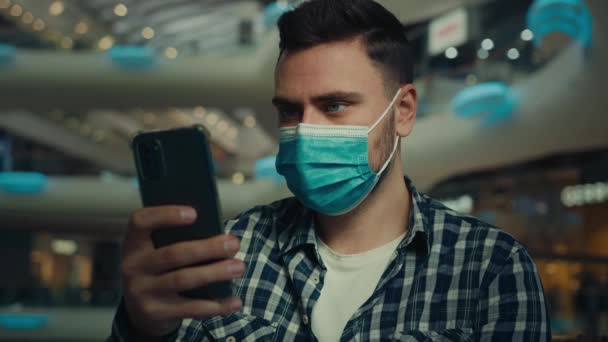 医療マスクのビジネスマン インターネット上でチャットアジアの男性は スマートフォンのスクロールインターネット上でオンラインチャット携帯電話を使用病気男性は ショッピングモール内のコロナウイルス感染検疫規則から顔を保護します — ストック動画