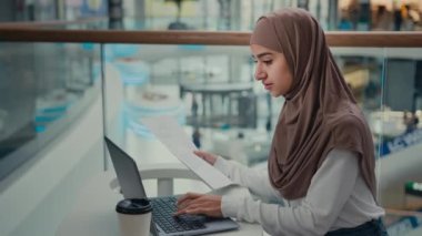 Genç kadın girişimci Arap Müslüman kadın tesettür işkadını kağıt işlerinde çalışıyor iş sözleşmeleri internet bankacılığı uygulaması e-ticaretinde faturaları ödeyen finansal belgeleri kontrol ediyor bilgisayardaki
