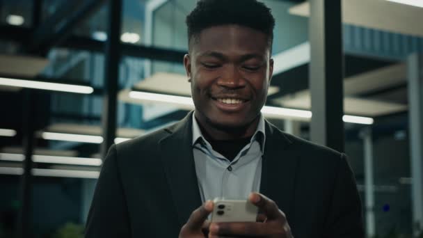 アフリカの実業家の若い男性起業家のユーザーエグゼクティブ労働者の従業員民族の男は 電話でメッセージをテキストメッセージ笑顔は良いモバイル通知を読むチャットオンラインビジネスチャットセル通信 — ストック動画
