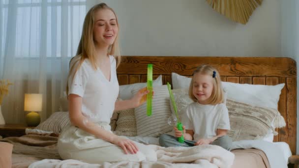 白种人妈妈妈妈带着小孩的小女孩妈妈宝宝收养了健康的女儿 在卧室里吹着肥皂泡坐在床上玩耍 一起在家里吹家庭保健保险 — 图库视频影像