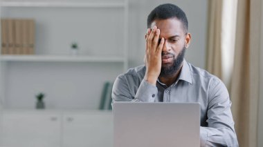 Stressed sick African American ethnic bearded man suffer with headache pain office worker businessman with laptop computer sad upset frustrated with bad news mistake error failure business problem