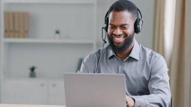 Gülümseyen mutlu Afro-Amerikalı etnik işadamı destek hattı menajeri, kulaklık takan internet servis öğretmeni web kameralı konferans görüşmesine uzaktan kumandalı internet üzerinden bakın.