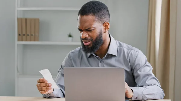 Worried upset African American ethnic man bearded businessman manage business company budget with calculator calculates counting expenses check bill payment loan income financial problems bankruptcy
