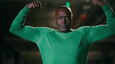 Olgun, sportif, komik, Afro-Amerikalı, kaslarını gösteren, kendine güvenen erkek sporcu eğitmeni, şişirilmiş pazı bisepsi gösteriyor.