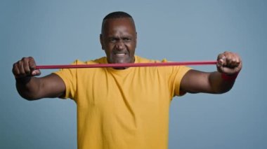 Olgun atletik adam gri arka plan stüdyosunda duruyor gergin ifadeli güçlü sporcu elastik bandı spor ekipmanları kullanarak esnetiyor güç kasları kasları spor konseptini gösteriyor