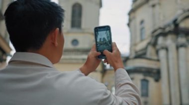 Male tourist taking pictures on smartphone makes photo in old city using mobile photography application man traveler enjoying cityscape takes picture on phone photographing landmark view from back