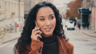 Close-up smiling happy cheerful 40s Hispanic Caucasian woman talking cell mobile phone in city with smile friendly conversation with friend boyfriend. Businesswoman lady answer call calling smartphone