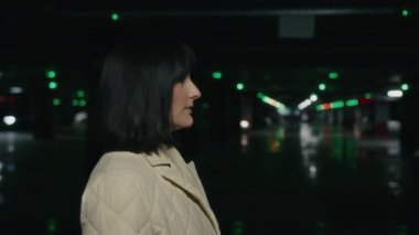 Caucasian multiethnic serious woman walk at parking lot side view. Millennial lady girl customer client female businesswoman walking at mall underground in darkness moving hurry to meeting in office
