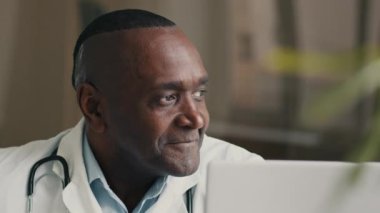 Happy middle-aged man doctor positive medical worker sits at hospital clinic cheerful smiling makes approval hand gesture okay agree winks one eye good recommendation satisfied with healthcare service