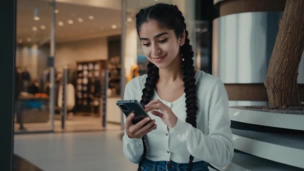 西班牙裔阿拉伯裔女商人坐在购物中心拿着电话在社交网络上聊天浏览网店下订单用智能手机手机软件发短信 — 图库视频影像