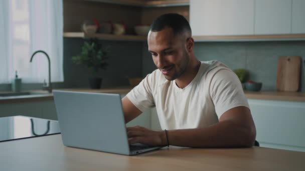 アフリカ千年紀の男多人種の男アメリカの男性ユーザーフリーランス自宅のキッチンデスクでノートパソコンを使用して作業遠くコンピュータアプリサービスでオンライン賭けゲームインターネットで購入するチャット — ストック動画