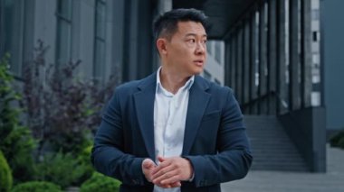 Angry worried middle-aged man 40s Asian Korean businessman standing in city looking at wristwatch check time waiting taxi worry about lateness late time hurry to business meeting inpatient male wait