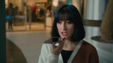 Caucasian woman indoors talking to phone AI talk record audio message with smartphone microphone voice recognition lady girl businesswoman speaking to mic loudspeaker cellphone recording smile laugh
