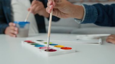 Close up acrylic watercolors colors pallet hands of unrecognizable ethnic African American boys kids schoolboys sons indoors children brothers friends painting together picture art paint lesson class