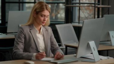 Caucasian middle-aged adult woman mature business female lady businesswoman entrepreneur in office write notes text in notebook on paper typing computer working accounting writing task ideas with pc