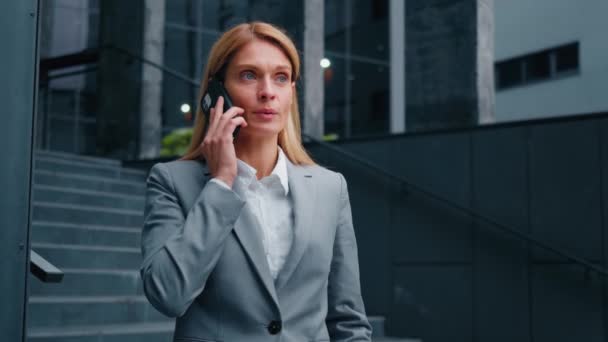 近くの企業ビルの外に立つ深刻な自信のある女性が携帯電話で会話ビジネスコールビジネス女性マネージャーセールスアシスタントリモート通信クライアントと携帯電話を使用して — ストック動画