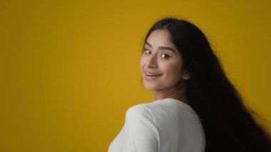 Portrait in yellow studio health female brunette with silky shiny soft long black dark hair showing perfect hairstyle Indian ethnic model woman with wavy curls hairdo hairstyling shampoo haircare