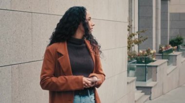 Sad worried Caucasian business woman girl female lady with mobile phone looking around peeps out someone waiting for taxi wait date late time need help upset with low battery problem alone in city