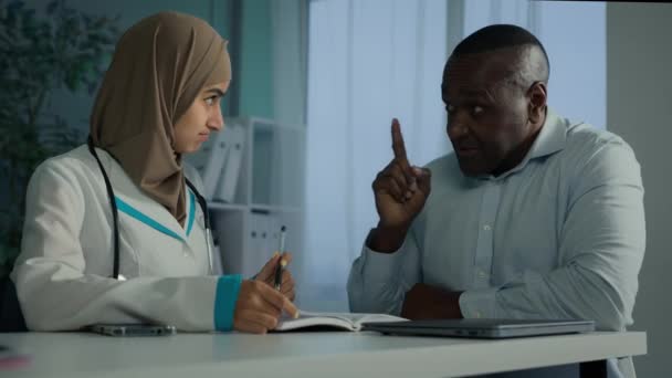 一般開業医ヒジャーブ州の女性若いイスラム教徒のアラビア人医師女性は アフリカの病気の男性に医療勧告を与えます古い患者は健康保険を記入健康テストの結果を記入するノートを作る — ストック動画