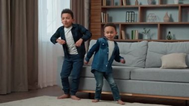 Ethnic African American multiethnic boys kids schoolboys pupils sons indoors children brothers friends dancing to song listen music celebrate party at home funny dance watching TV moving having fun