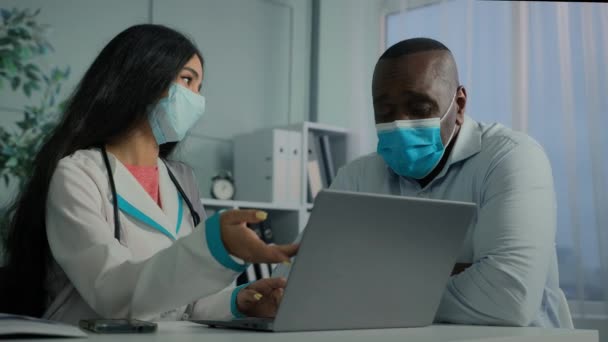 若い医師の女性は マスク使用中の老人患者と話しますラップトップチェック電子健康テスト結果サービスオンライン医学は コンピュータ上の高齢者のクライアントを登録します近代的な技術は 医療勧告を与えます — ストック動画