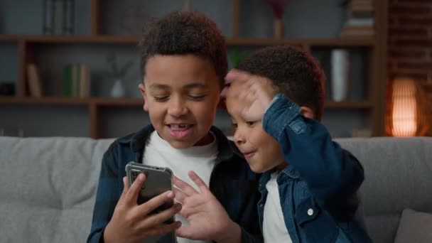 エスニック アフリカ系アメリカ人多人種間の男の子子供学校の息子屋内でホーム子供兄弟友人でホームトーキングビデオチャットコールの会話挨拶こんにちはオンラインチャットとスマートフォン — ストック動画