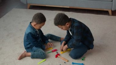 Ethnic African American multiracial multiethnic boys kids schoolboys pupils sons indoors at home children brothers cousins friends on floor carpet play with toys tools playing repair game together