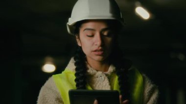 Young arabian woman technician inspector engineer developer wears protecting helmet uniform use electronic digital tablet checking manufacture work inspecting engineering measures make business plan