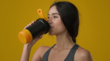 Portrait female in yellow studio drinking water enjoy hydration ethnic Indian strong sporty girl with bottle refreshment athlete sport woman drink supplement protein liquid calcium smile to camera