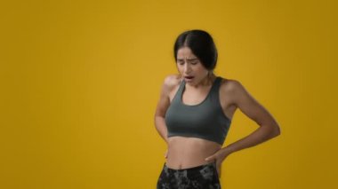 Sad upset suffering Indian slim athlete sporty woman in studio yellow background unwell girl model sports lady feeling backache abdominal aching pain in spine belly painful menstrual period cramp